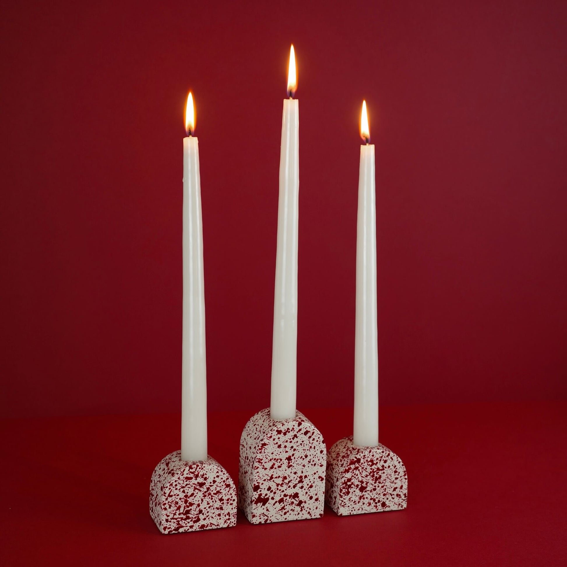 Burgundy paint splattered on a cream concrete arch shaped candleholder, pair