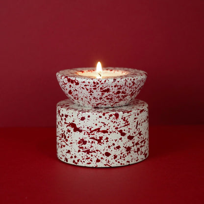 Burgundy paint splattered on a cream concrete half sphere shaped tealight holder, stacked on a cylinder tealight holder