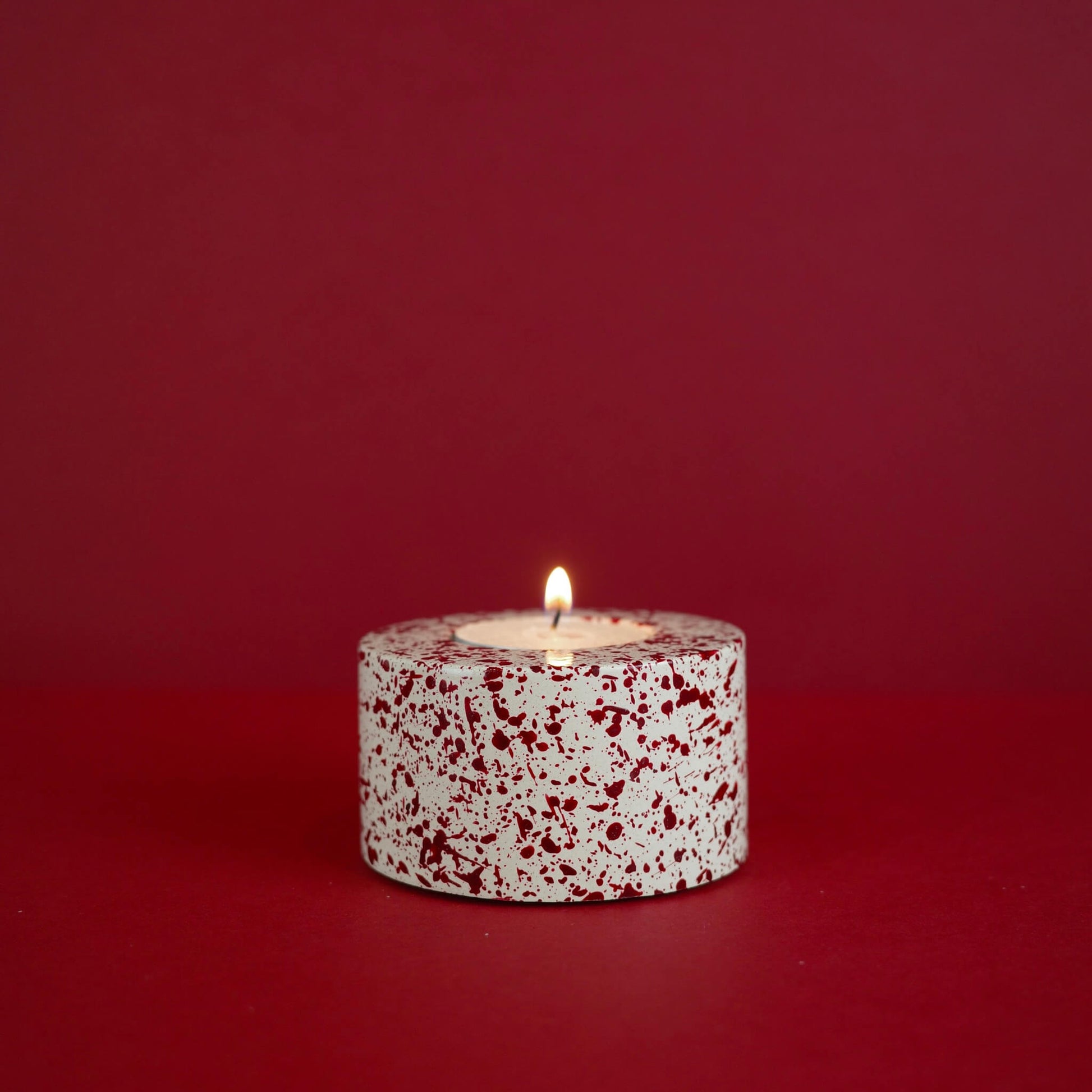 Burgundy paint splattered on a cream concrete cylinder tealight holder