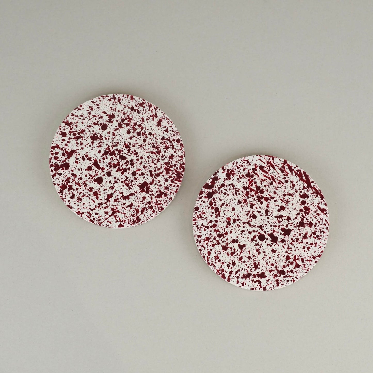 Burgundy paint splattered on a cream concrete circle round coaster set of 2