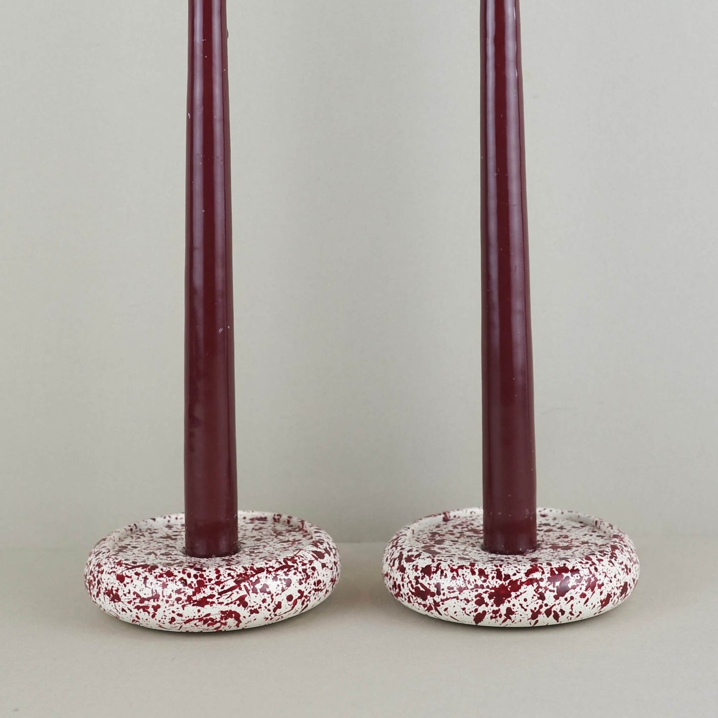 Burgundy paint splattered on a cream concrete circle shaped candleholder, stackable, close up