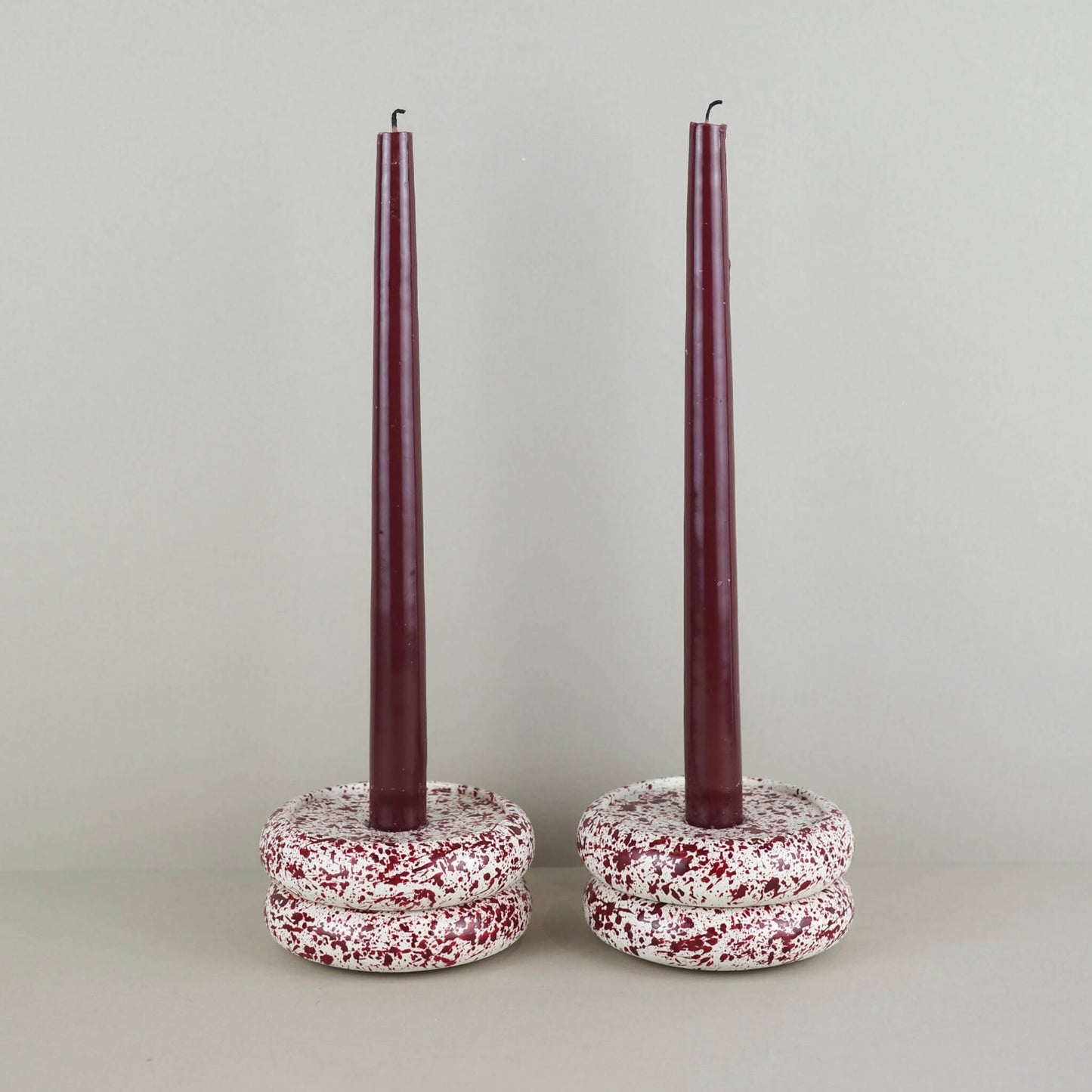 Burgundy paint splattered on a cream concrete circle shaped candleholder, pair, 2 stacked on top of each other