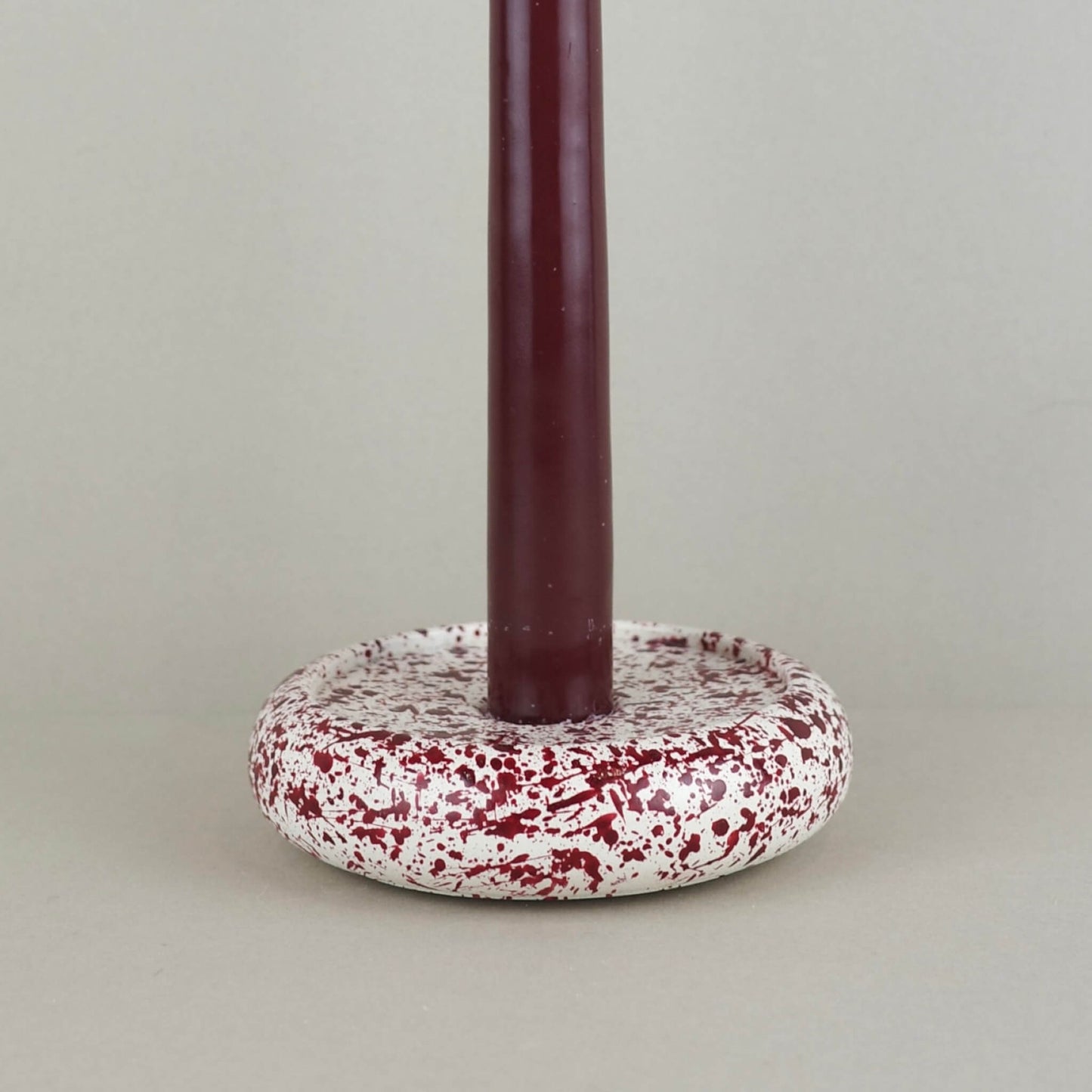 Burgundy paint splattered on a cream concrete circle shaped candleholder, stackable, close up