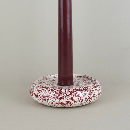 Burgundy paint splattered on a cream concrete circle shaped candleholder, stackable, close up