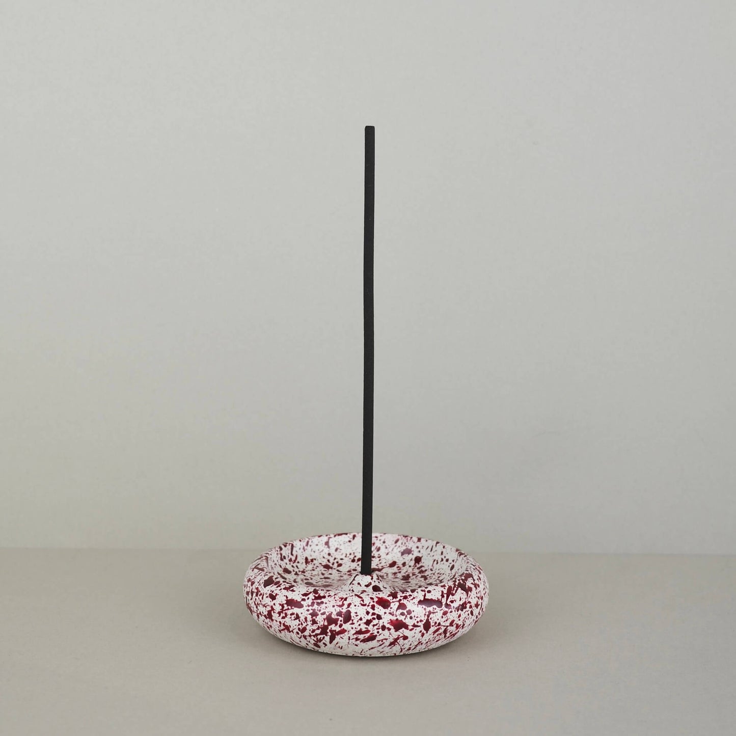 Burgundy paint splattered on a cream concrete circle shaped incense holder stackable