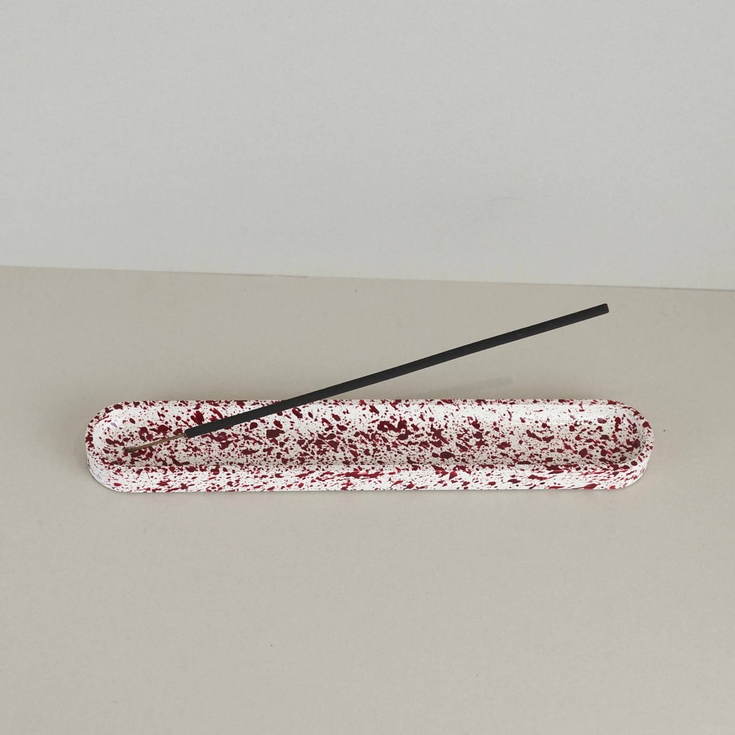 Burgundy paint splattered on a cream concrete long oblong incense holder, top view