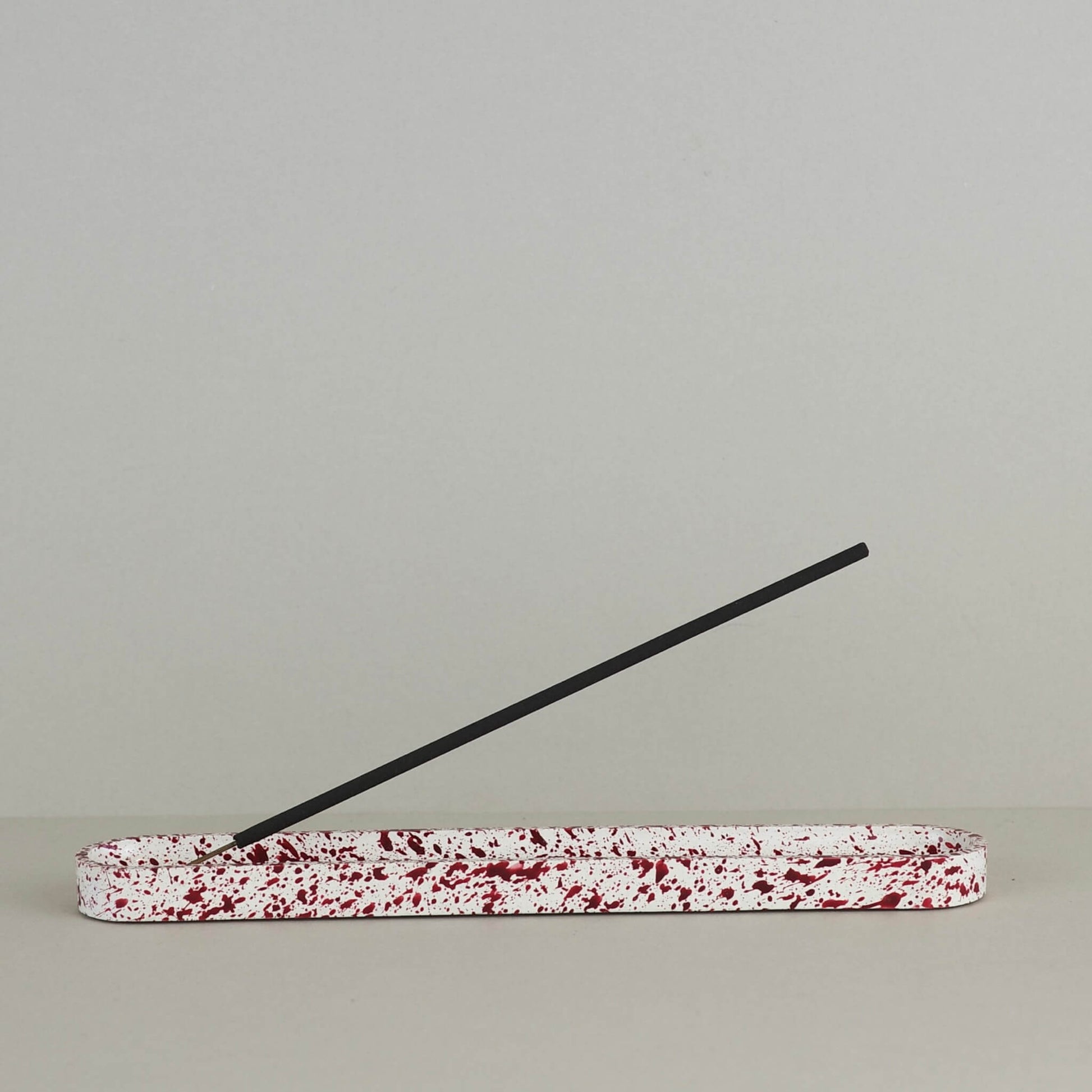 Burgundy paint splattered on a cream concrete long oblong incense holder