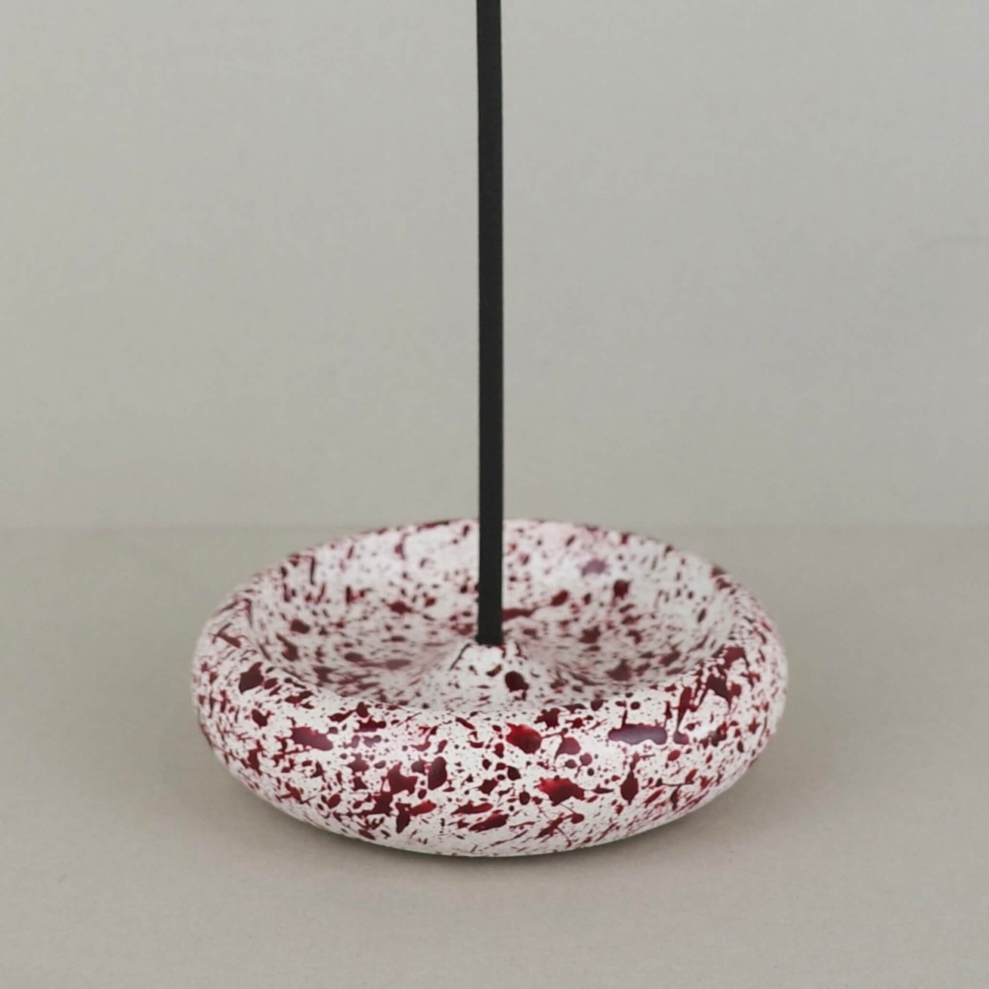 Burgundy paint splattered on a cream concrete circle shaped incense holder stackable, close up