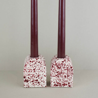 Burgundy paint splattered on a cream concrete large arch shaped candleholder, pair, close up