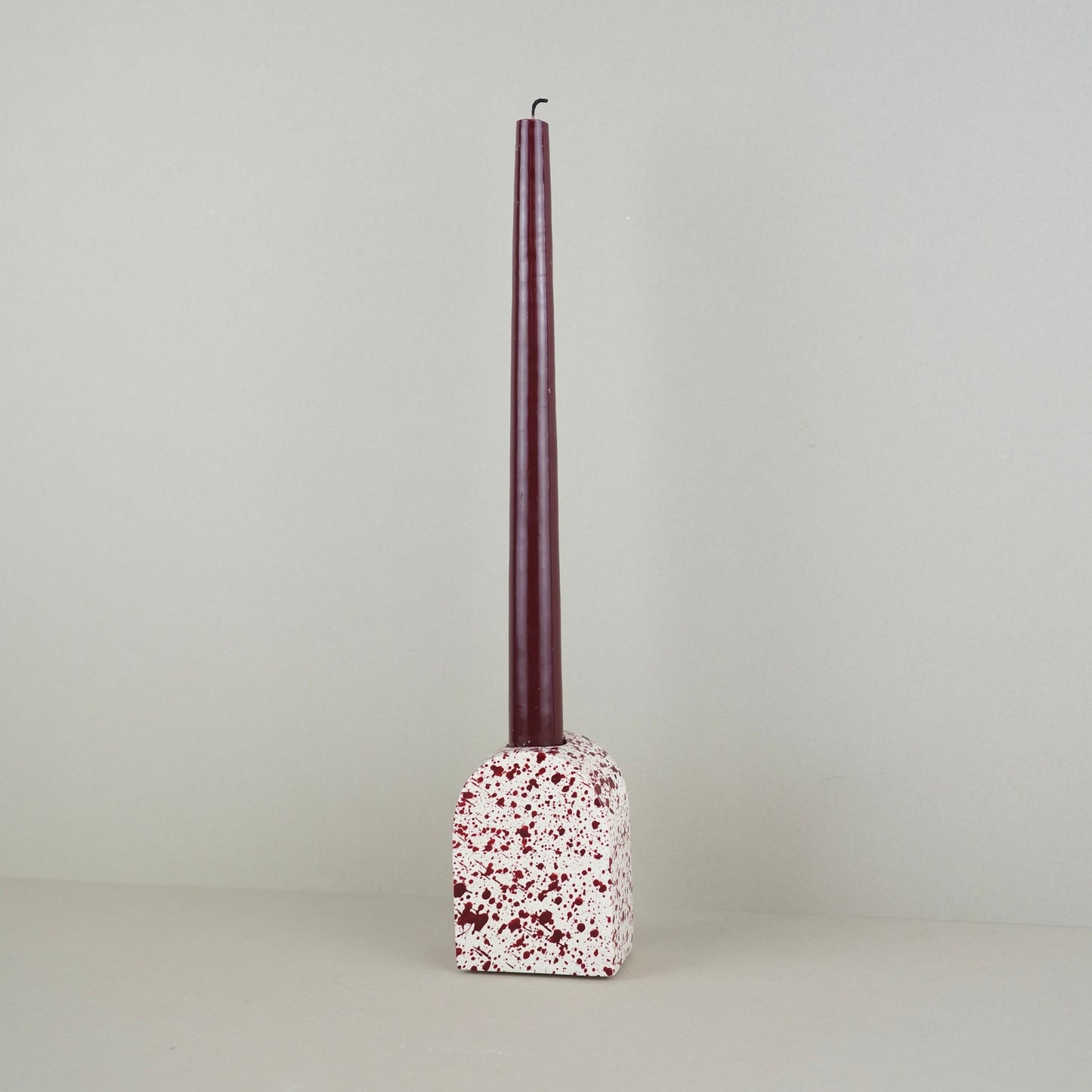 Burgundy paint splattered on a cream concrete large arch shaped candleholder