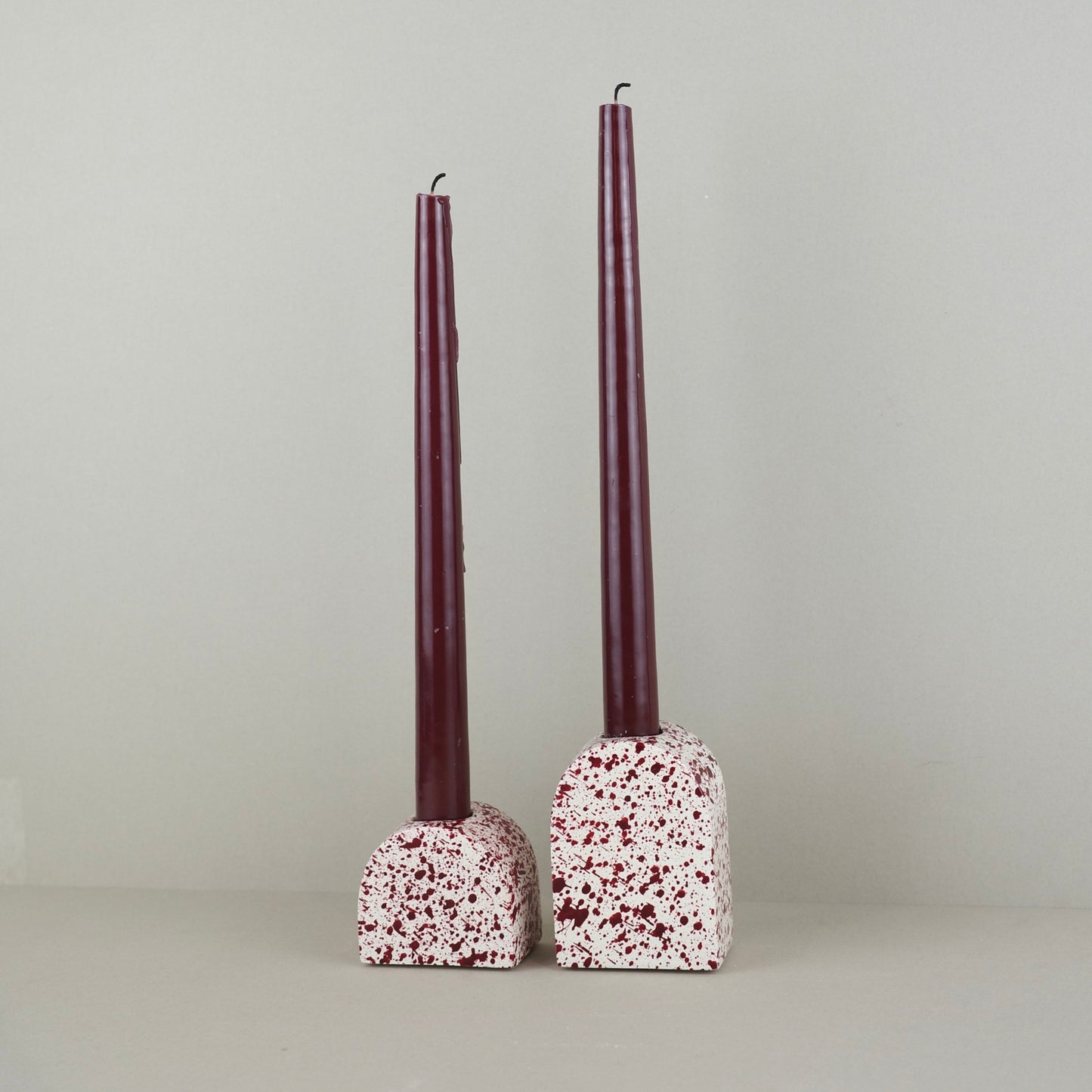 Burgundy paint splattered on a cream concrete small and large arch shaped candleholder