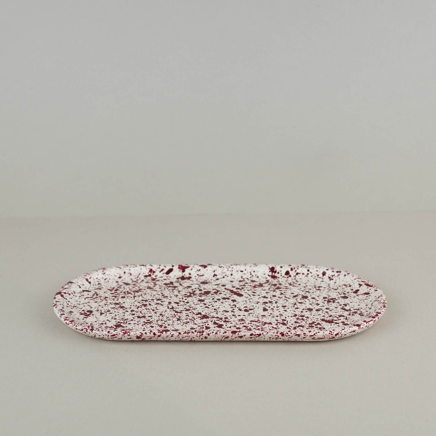 Burgundy paint splattered on a cream concrete oblong thin decorative tray