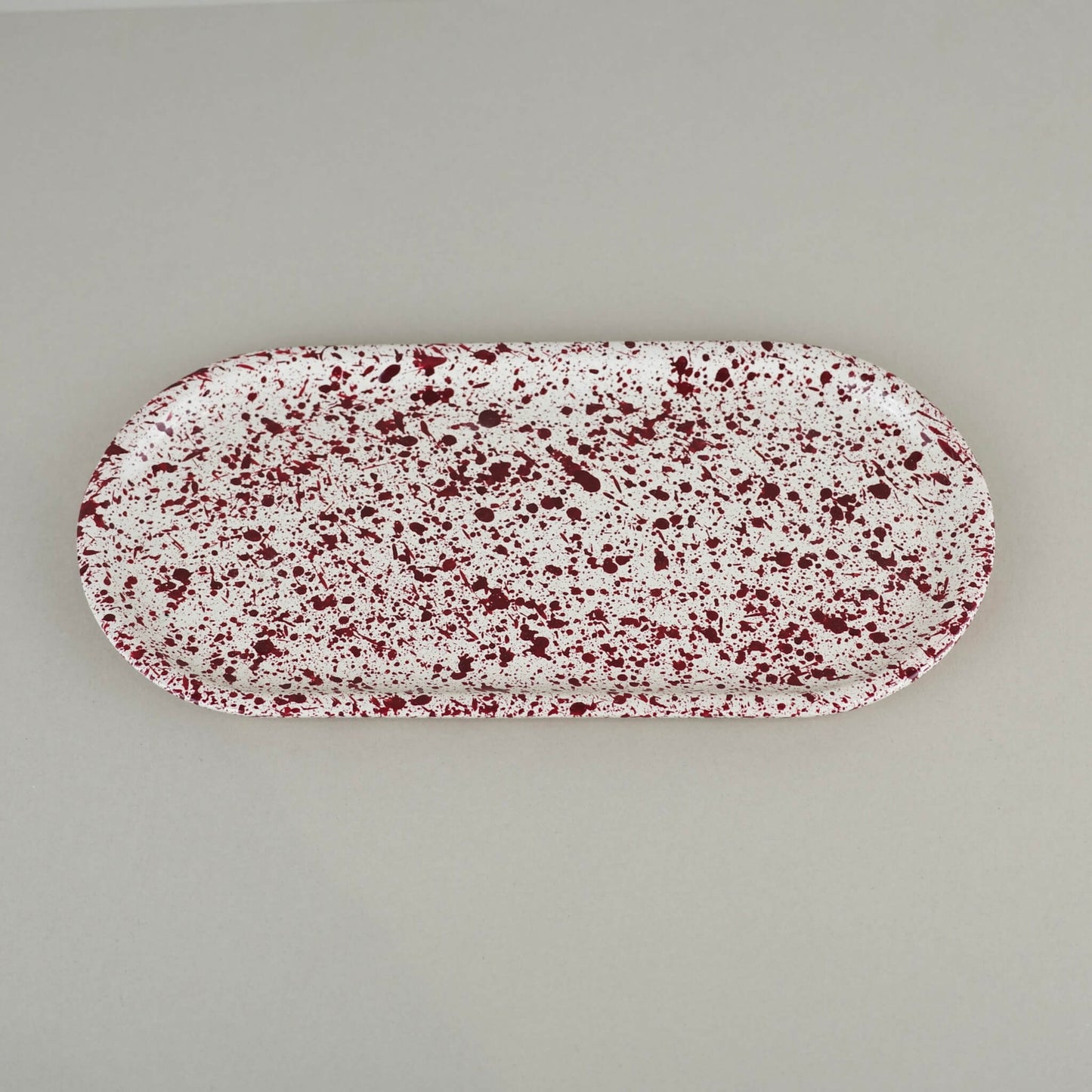 Burgundy paint splattered on a cream concrete oblong thin decorative tray top view