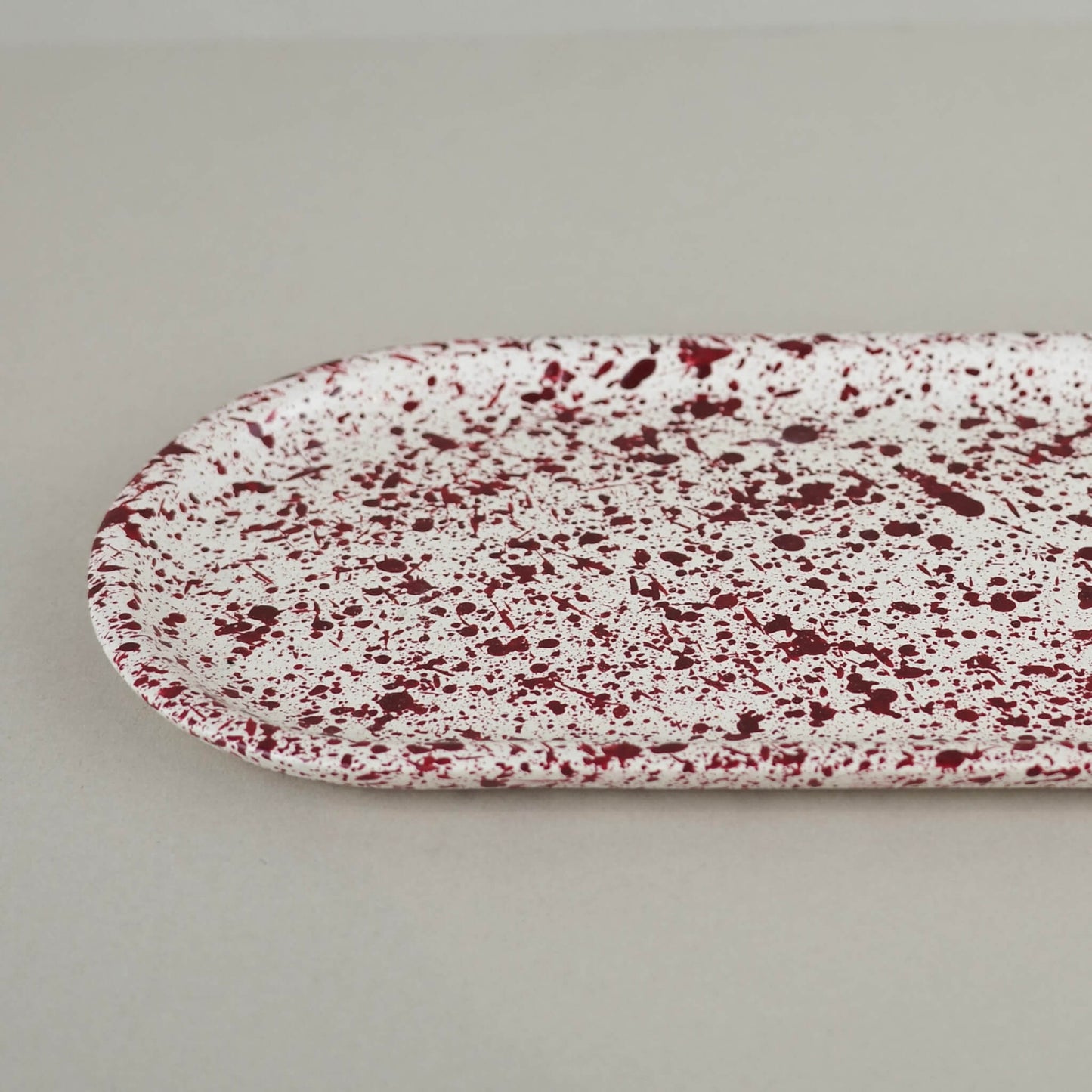 Burgundy paint splattered on a cream concrete oblong thin decorative tray, close up view