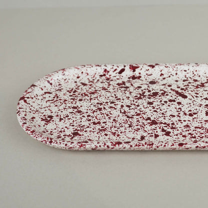 Burgundy paint splattered on a cream concrete oblong thin decorative tray, close up view