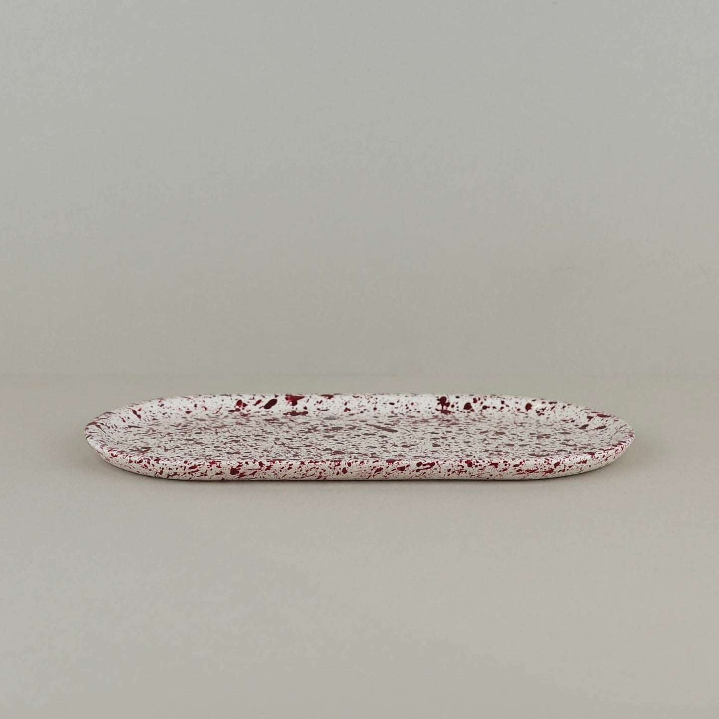 Burgundy paint splattered on a cream concrete oblong thin decorative tray