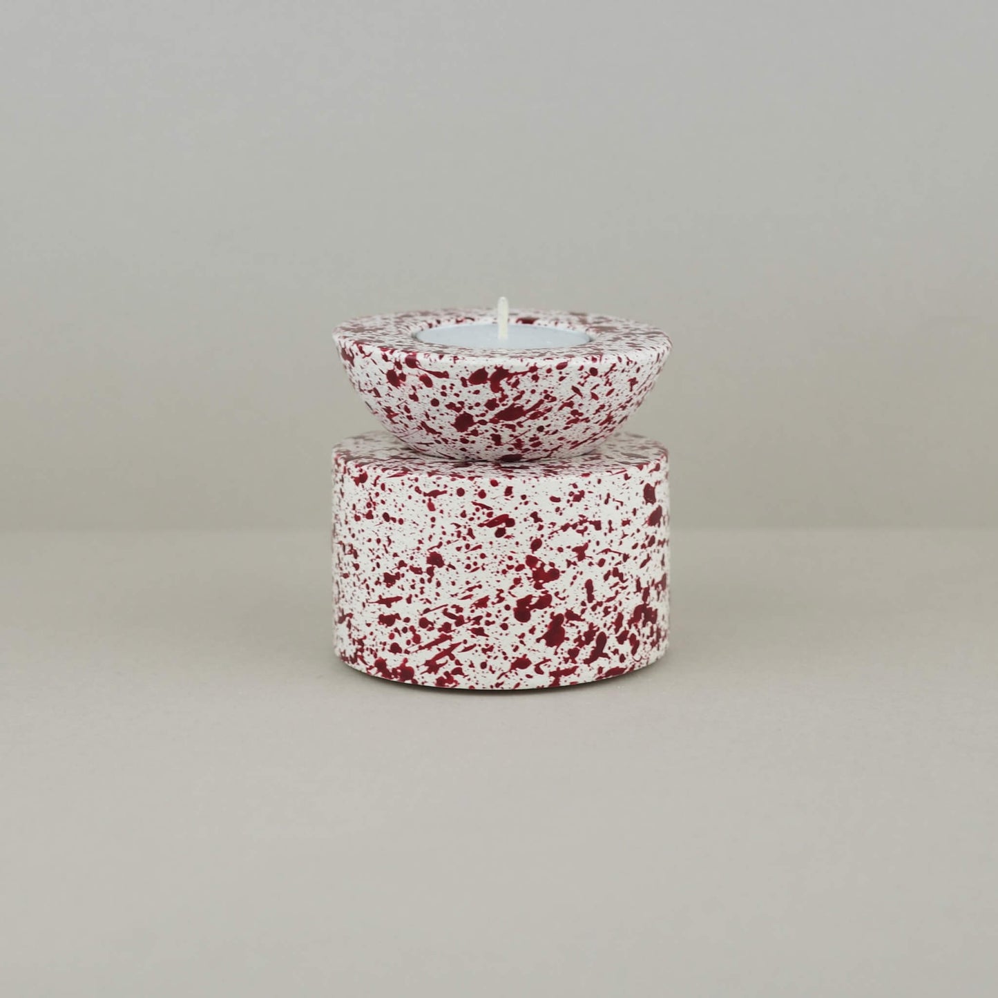 Burgundy paint splattered on a cream concrete half sphere shaped tealight holder, stacked on a cylinder tealight holder