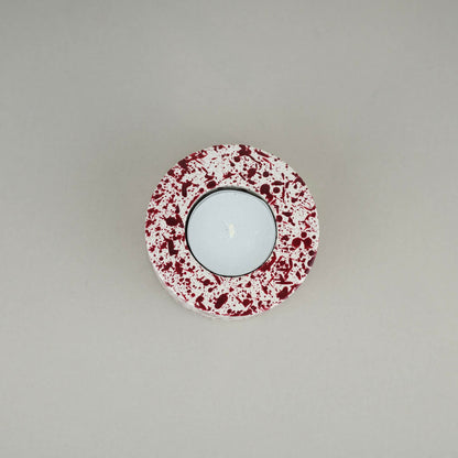 Burgundy paint splattered on a cream concrete cylinder tealight holder top view