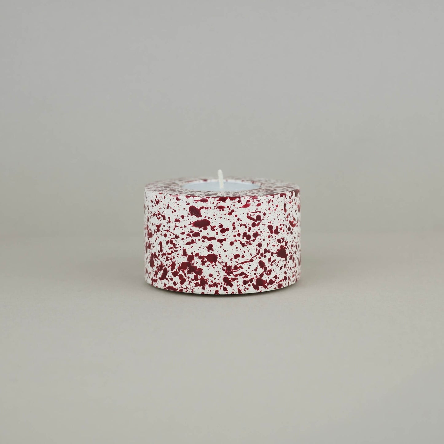 Burgundy paint splattered on a cream concrete cylinder tealight holder
