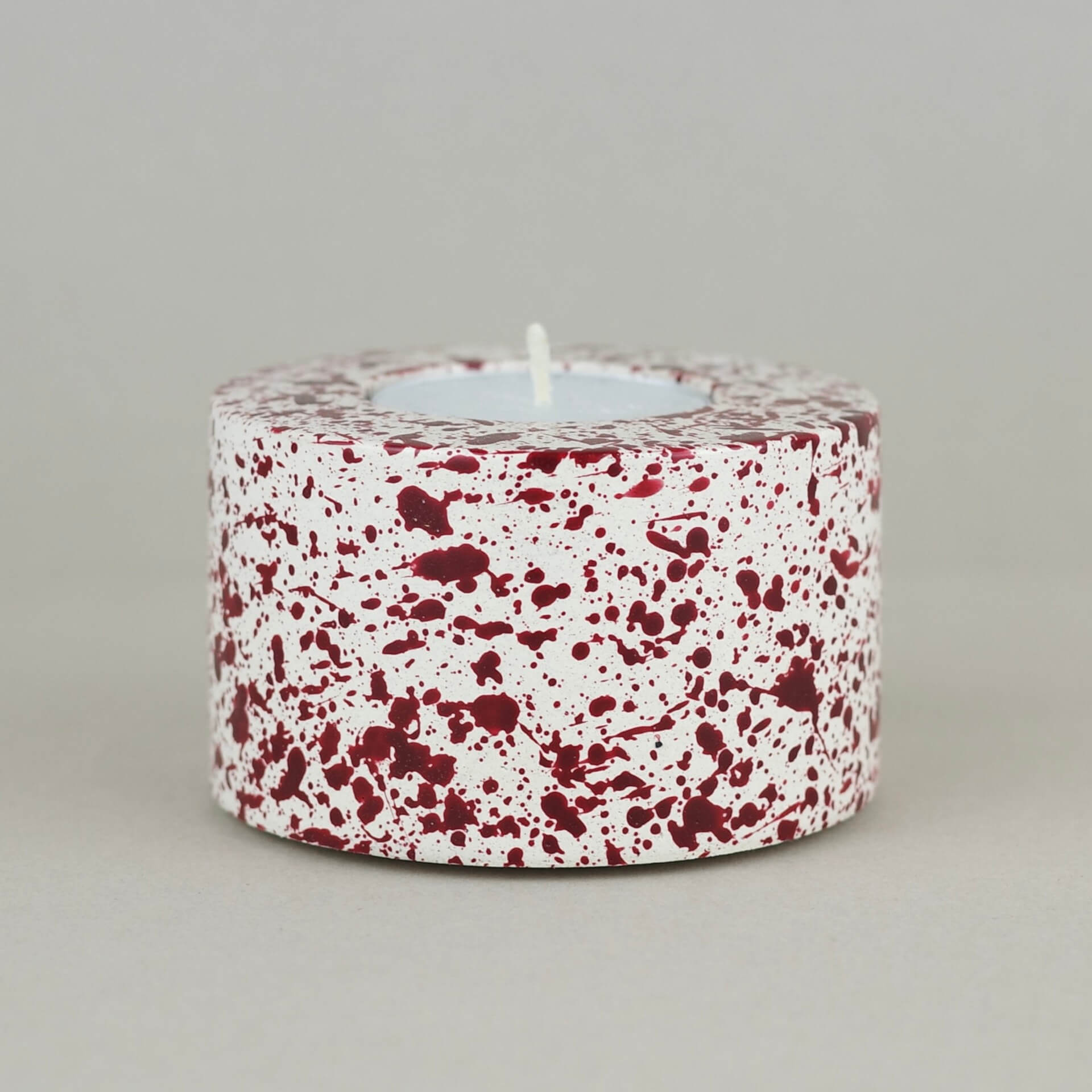 Burgundy paint splattered on a cream concrete cylinder tealight holder