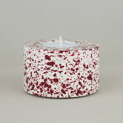 Burgundy paint splattered on a cream concrete cylinder tealight holder