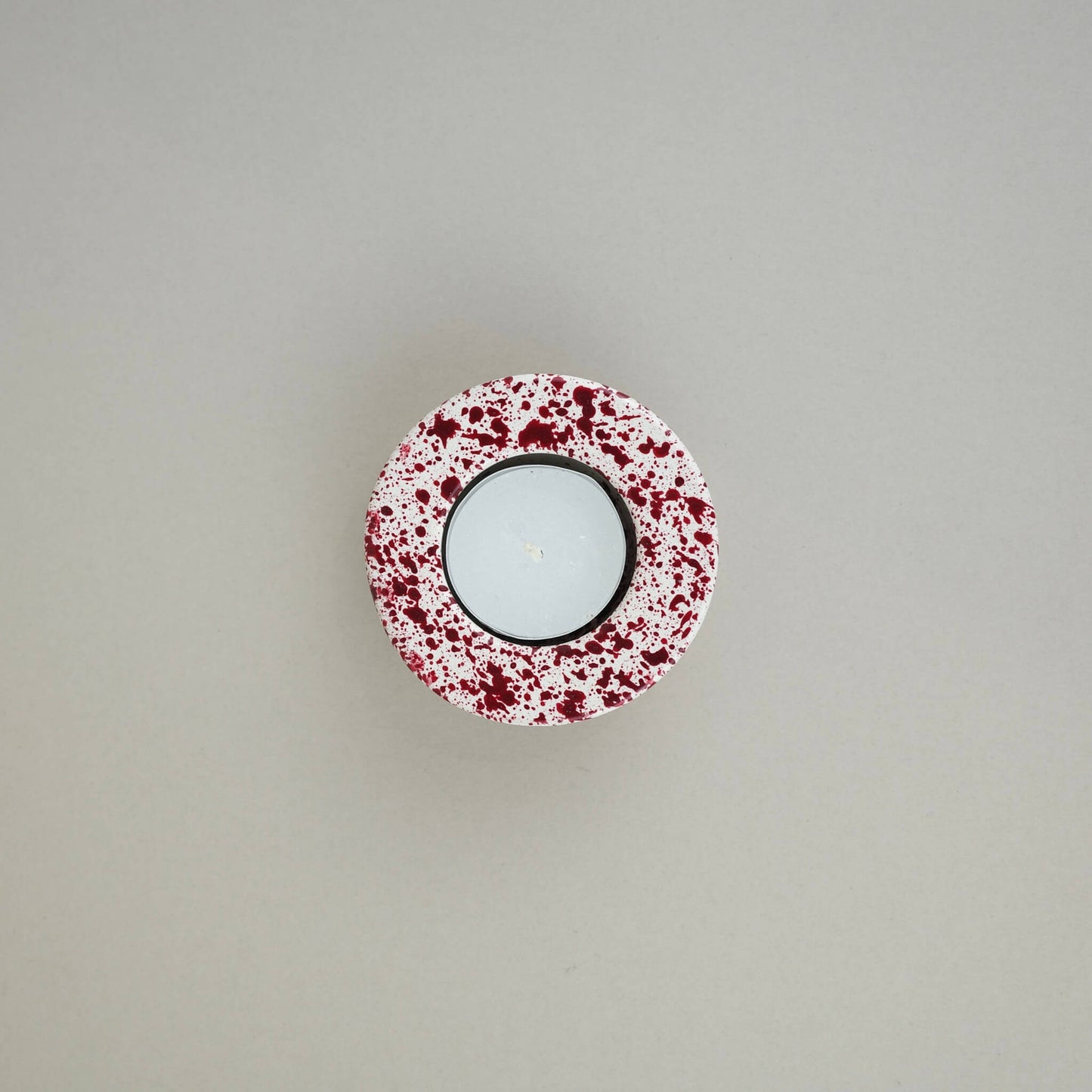 Burgundy paint splattered on a cream concrete half sphere shaped tealight holder top view