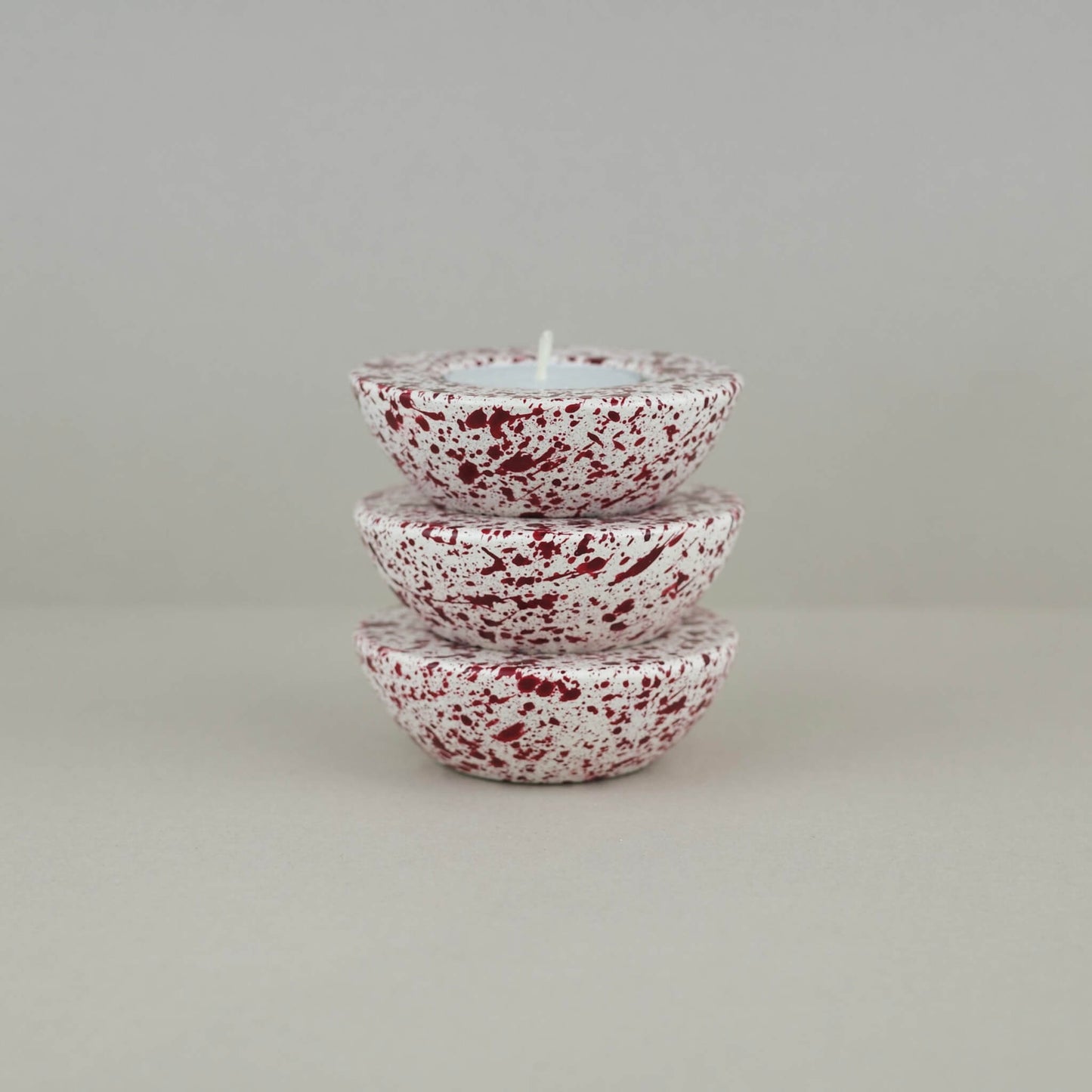 Burgundy paint splattered on a cream concrete half sphere shaped tealight holder three stacked on top of each other