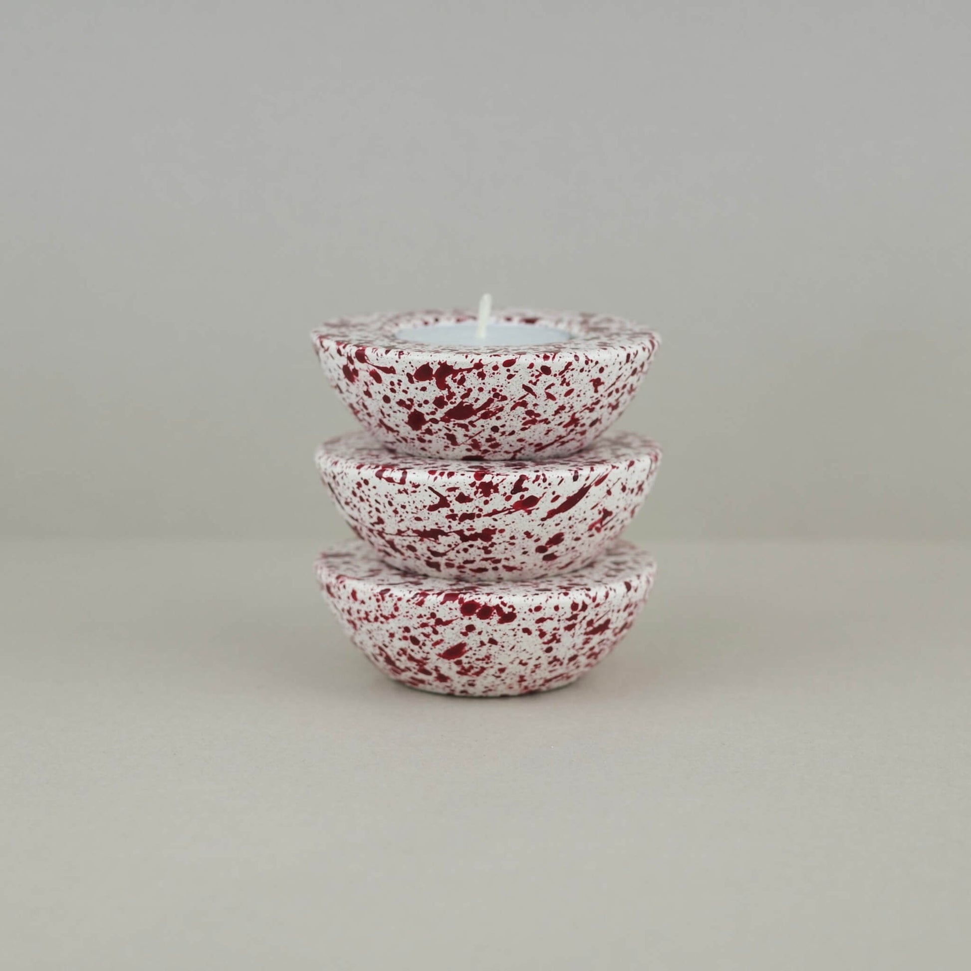 Burgundy paint splattered on a cream concrete half sphere shaped tealight holder three stacked on top of each other