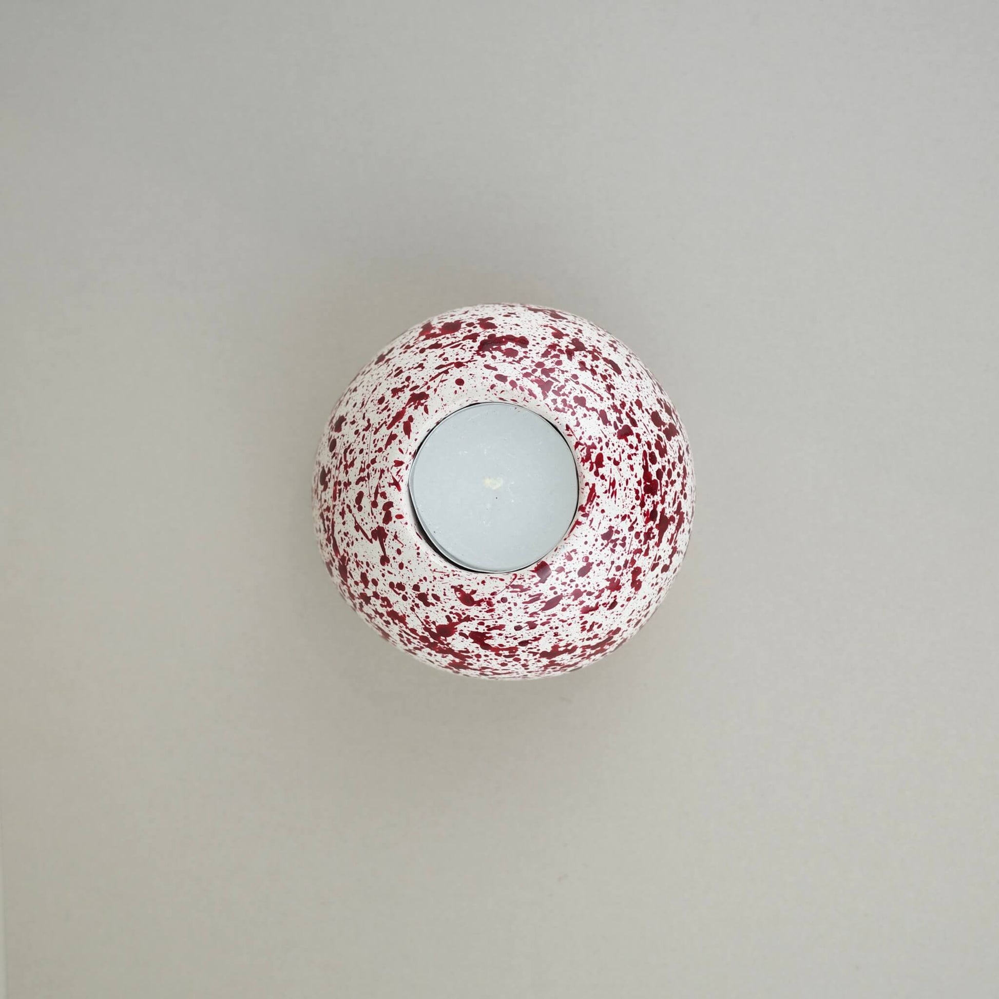 Burgundy paint splattered on a cream concrete sphere shaped tealight holder top view