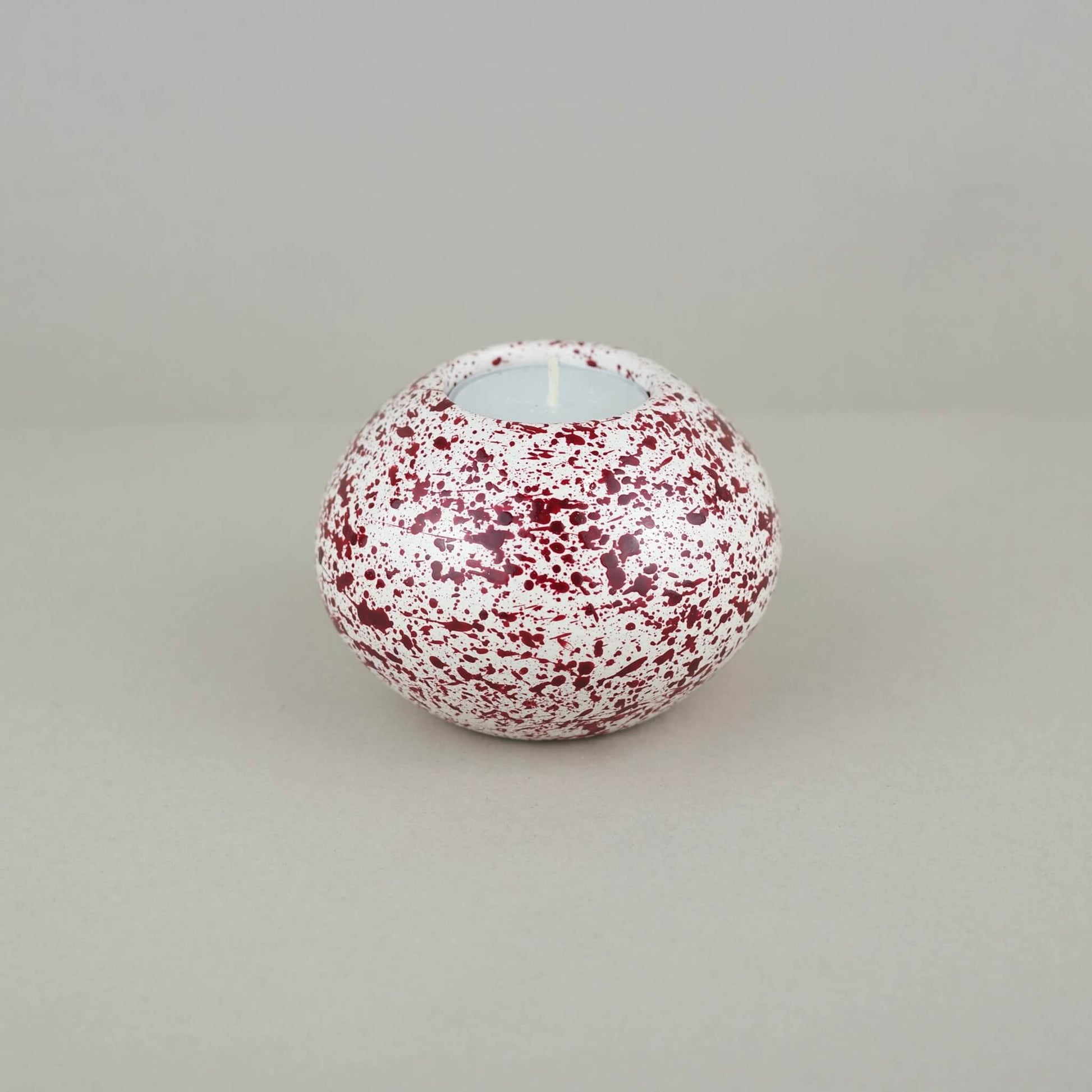 Burgundy paint splattered on a cream concrete sphere shaped tealight holder