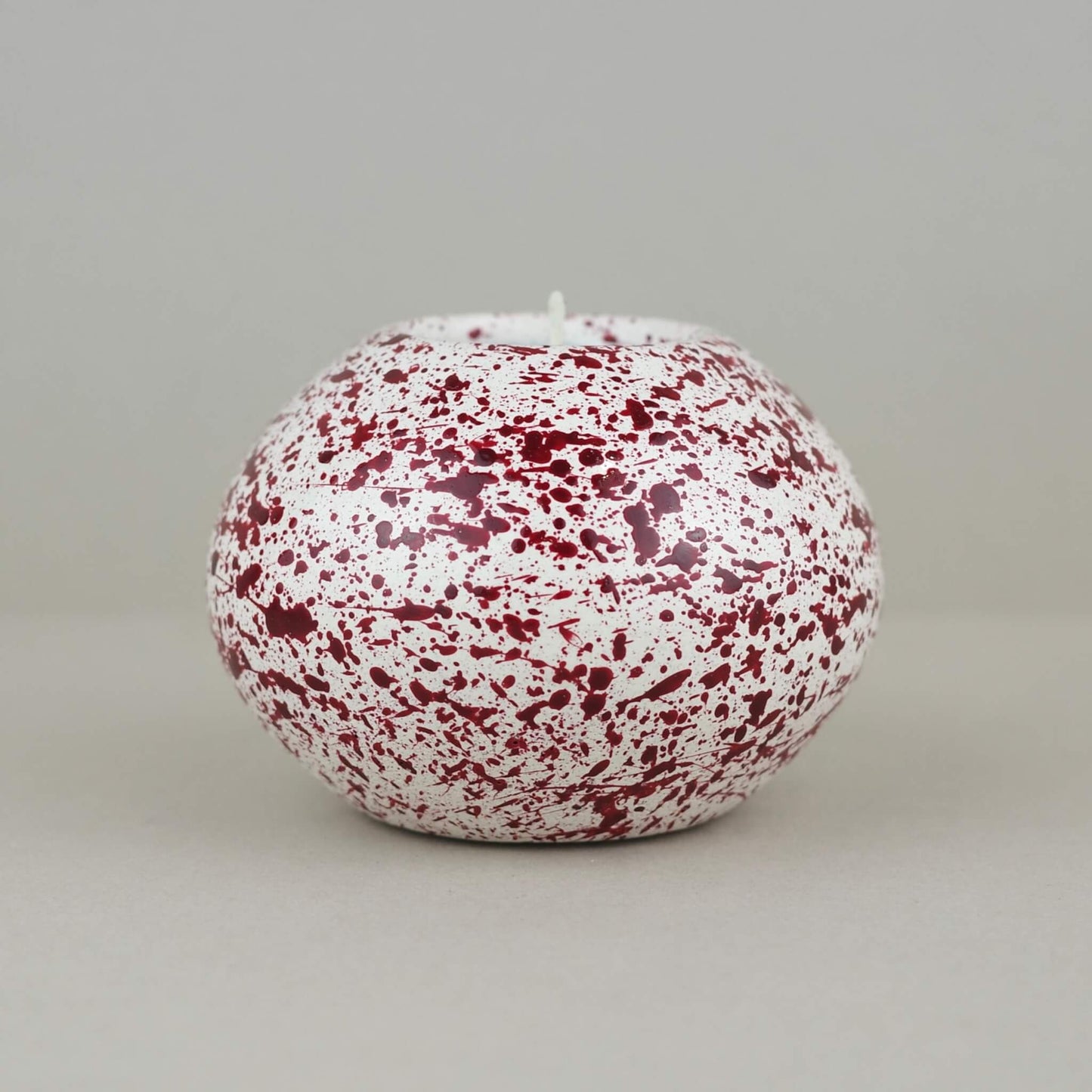 Burgundy paint splattered on a cream concrete sphere shaped tealight holder close up