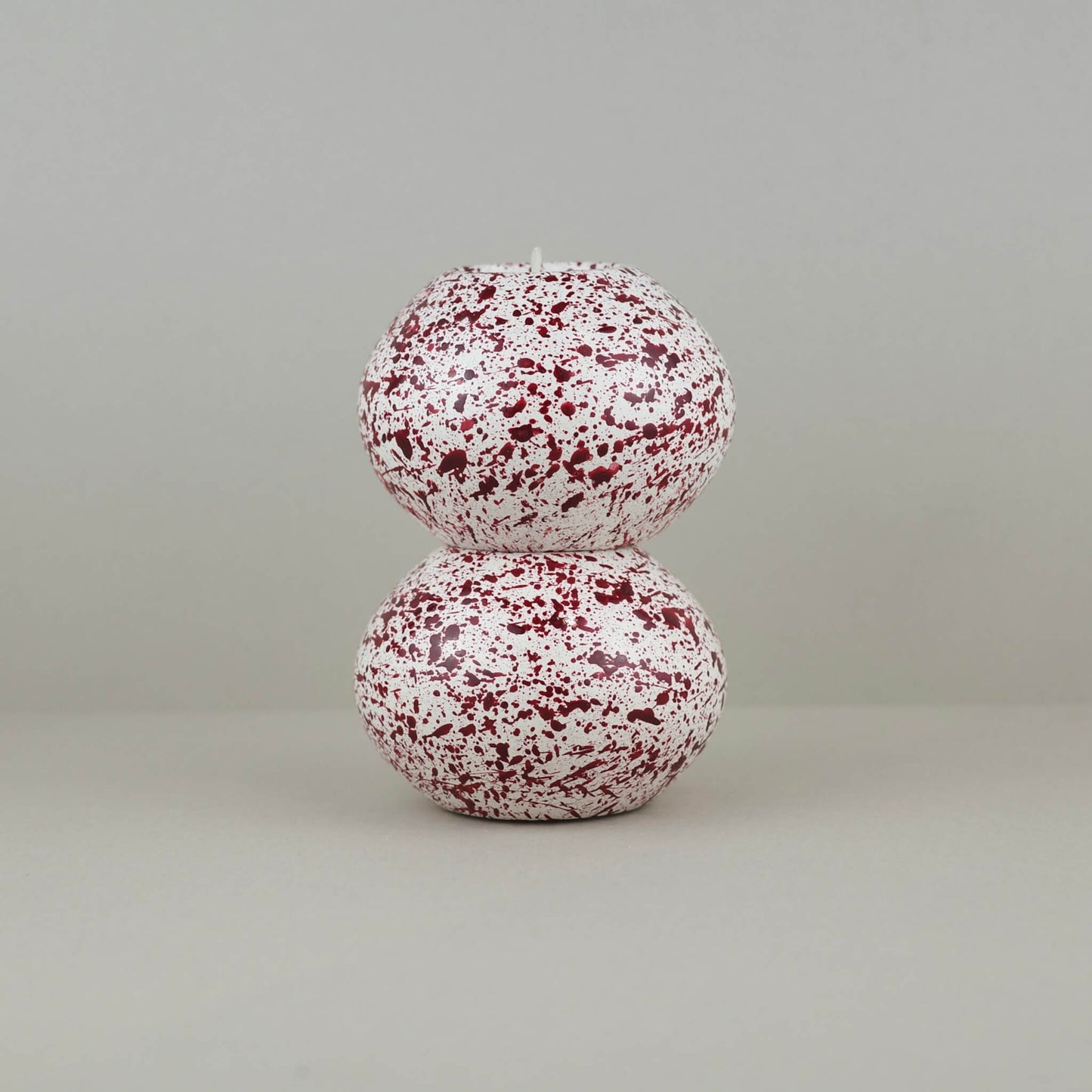 Burgundy paint splattered on a cream concrete sphere shaped tealight holder, two stacked on top of each other