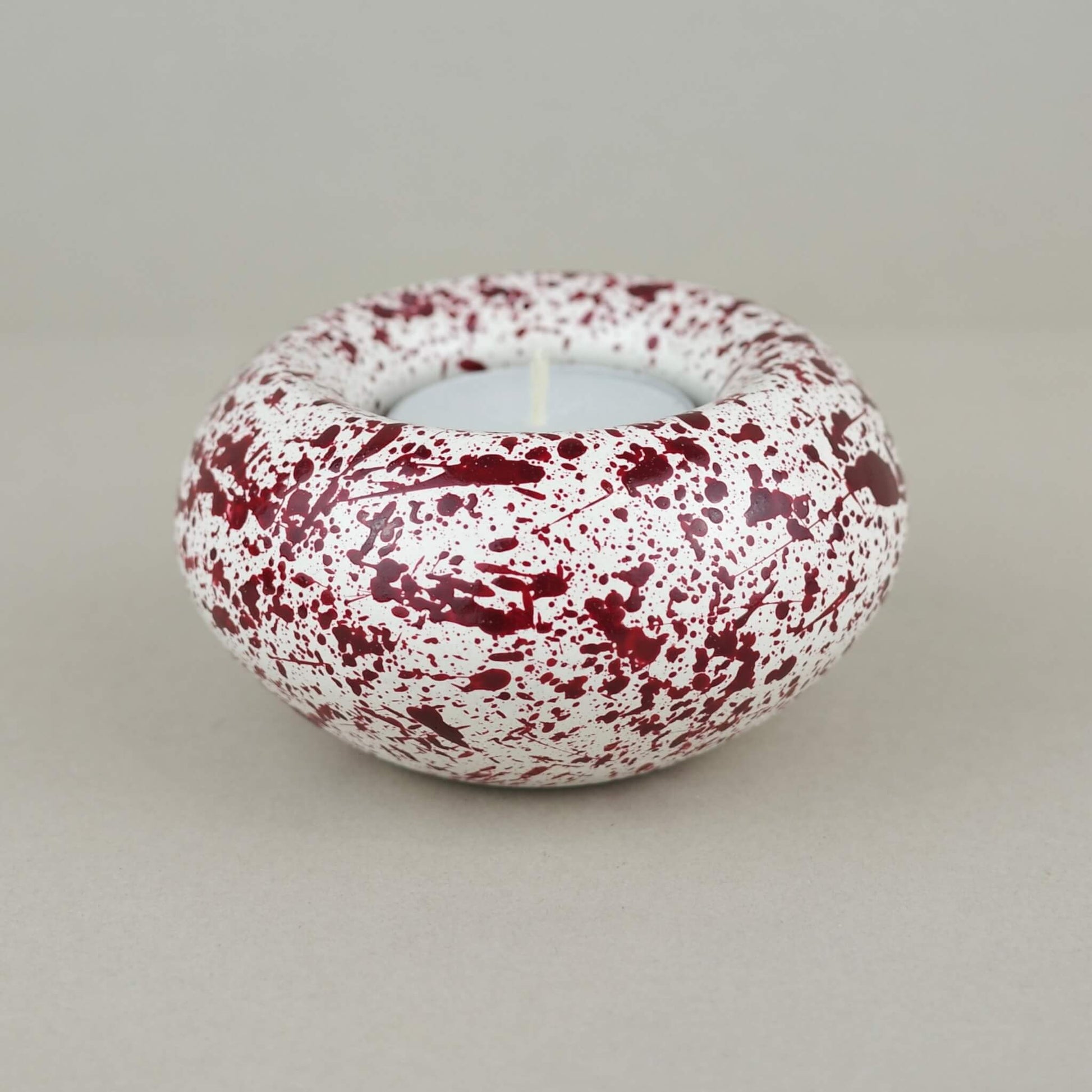 Burgundy paint splattered on a cream concrete sunken sphere shaped tealight holder