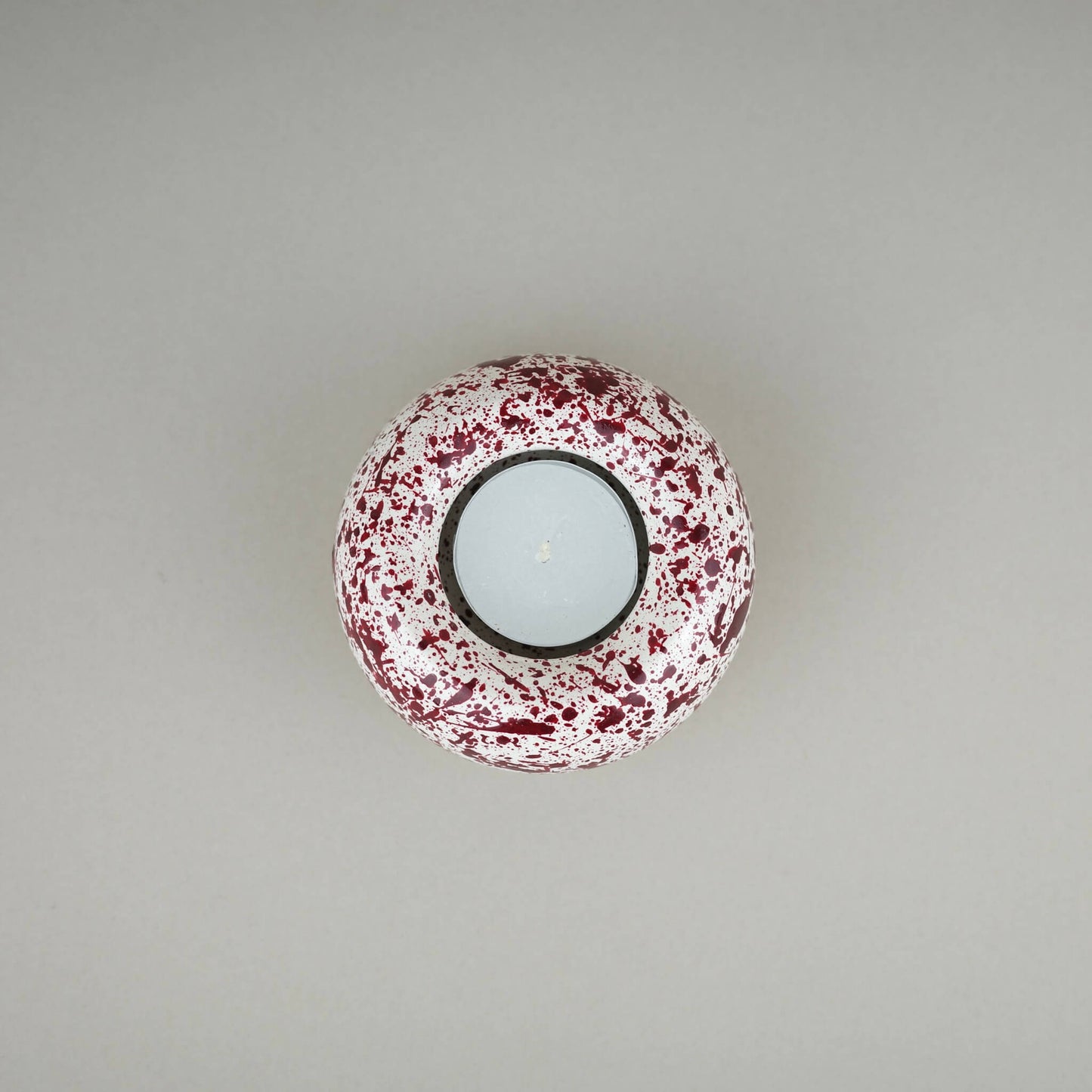 Burgundy paint splattered on a cream concrete sunken sphere shaped tealight holder top view