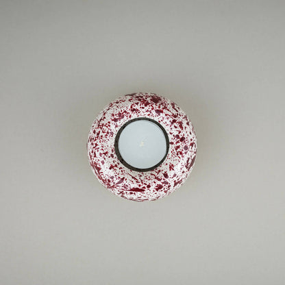 Burgundy paint splattered on a cream concrete sunken sphere shaped tealight holder top view