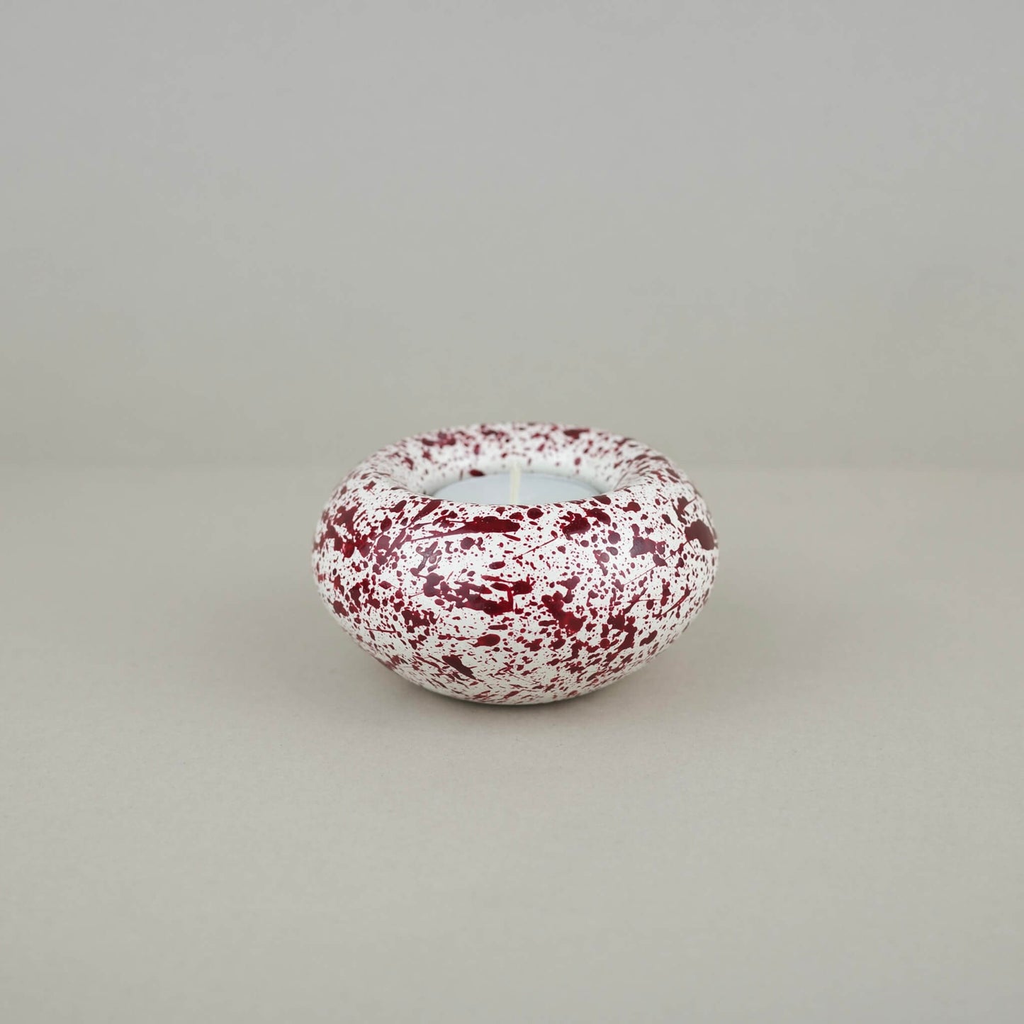 Burgundy paint splattered on a cream concrete sunken sphere shaped tealight holder