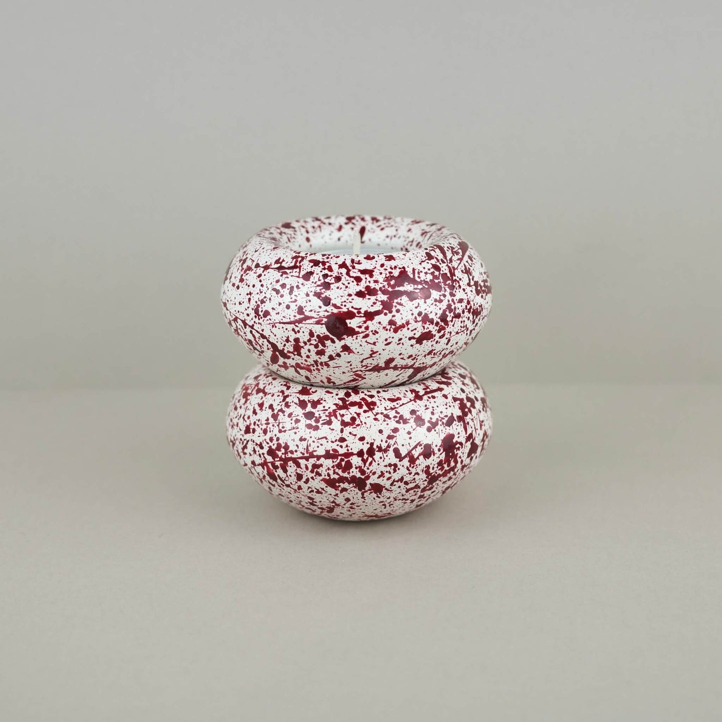 Burgundy paint splattered on a cream concrete sunken sphere shaped tealight holder 2 stacked on top of each other