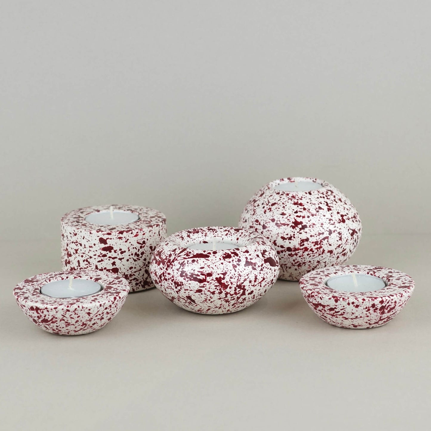 Burgundy paint splattered on a cream concrete tealight holder, collection of sphere shapes