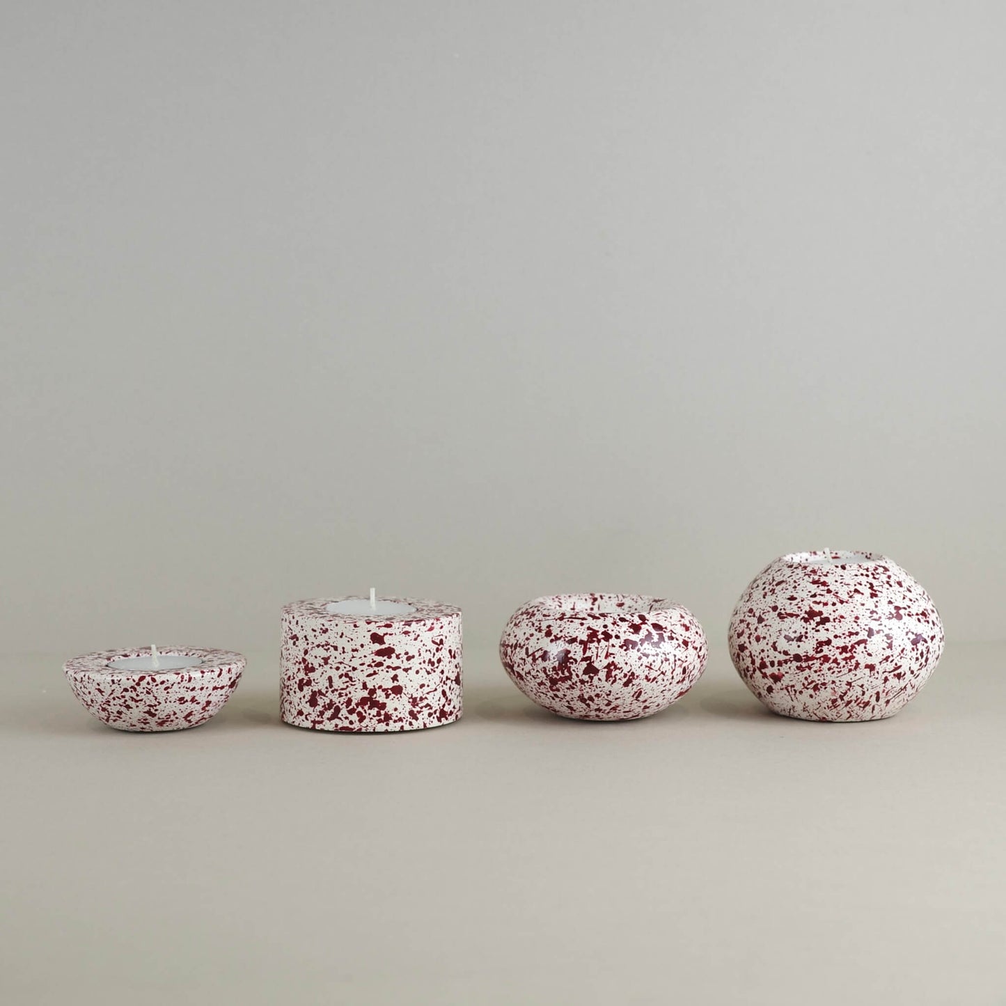 Burgundy paint splattered on a cream concrete tealight holder, collection of sphere shapes