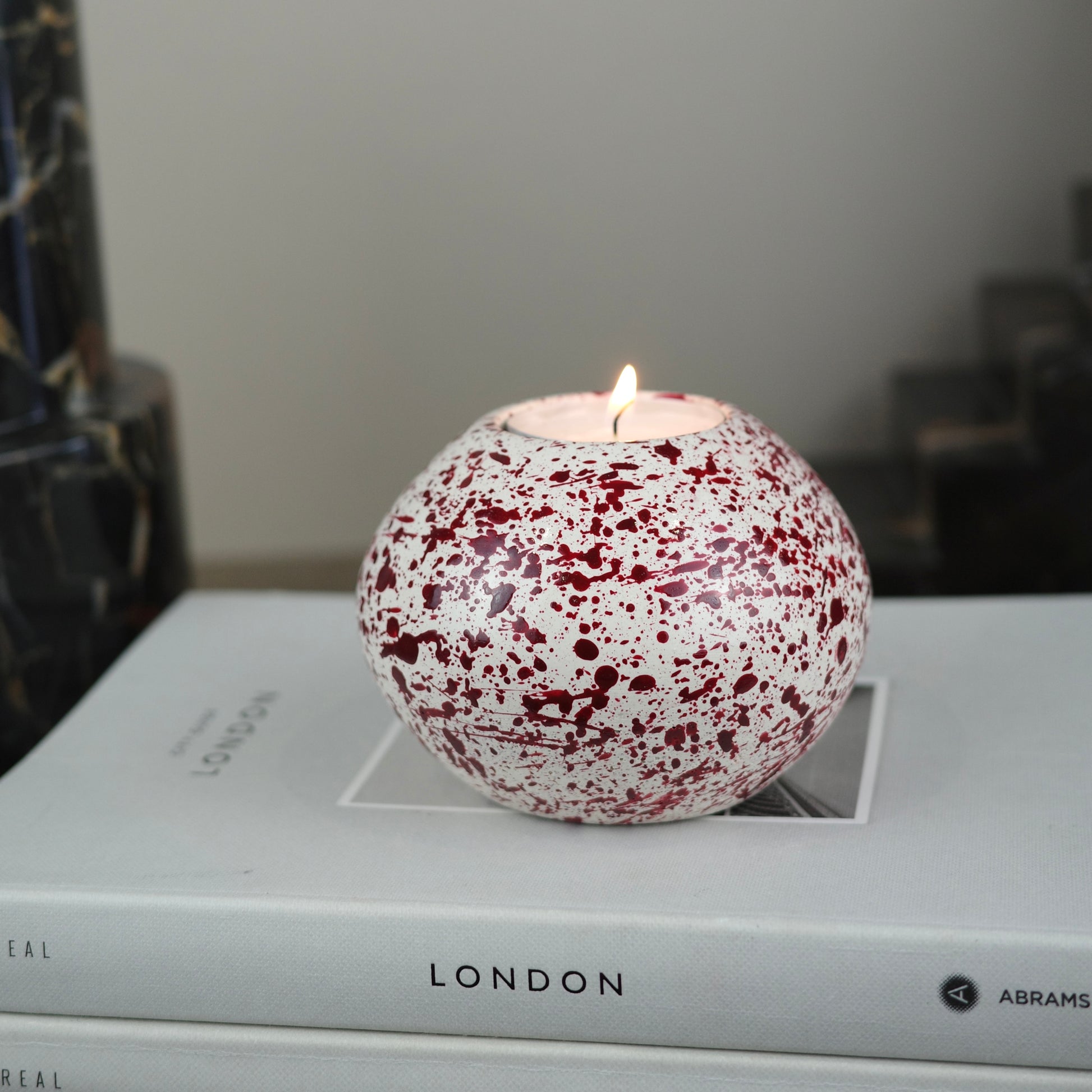 Burgundy paint splattered on a cream concrete sphere shaped tealight holder