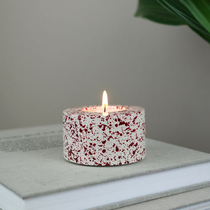 Burgundy paint splattered on a cream concrete cylinder tealight holder
