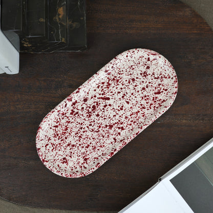 Burgundy paint splattered on a cream concrete oblong thin decorative tray top view