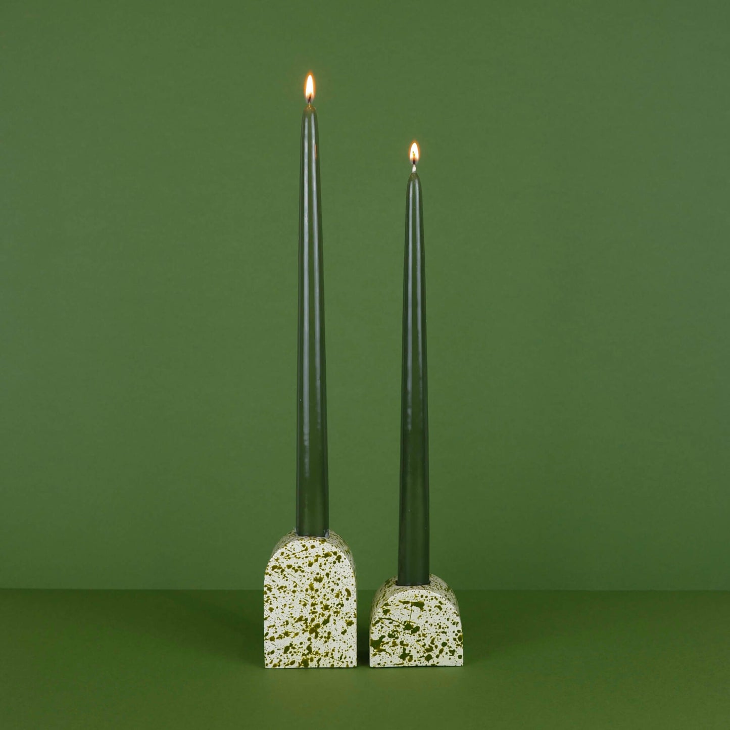 Green paint splattered on a cream concrete large arch shaped candleholder, pair