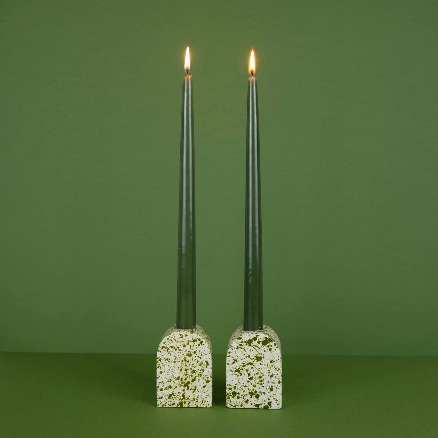 Green paint splattered on a cream concrete large arch shaped candleholder, pair