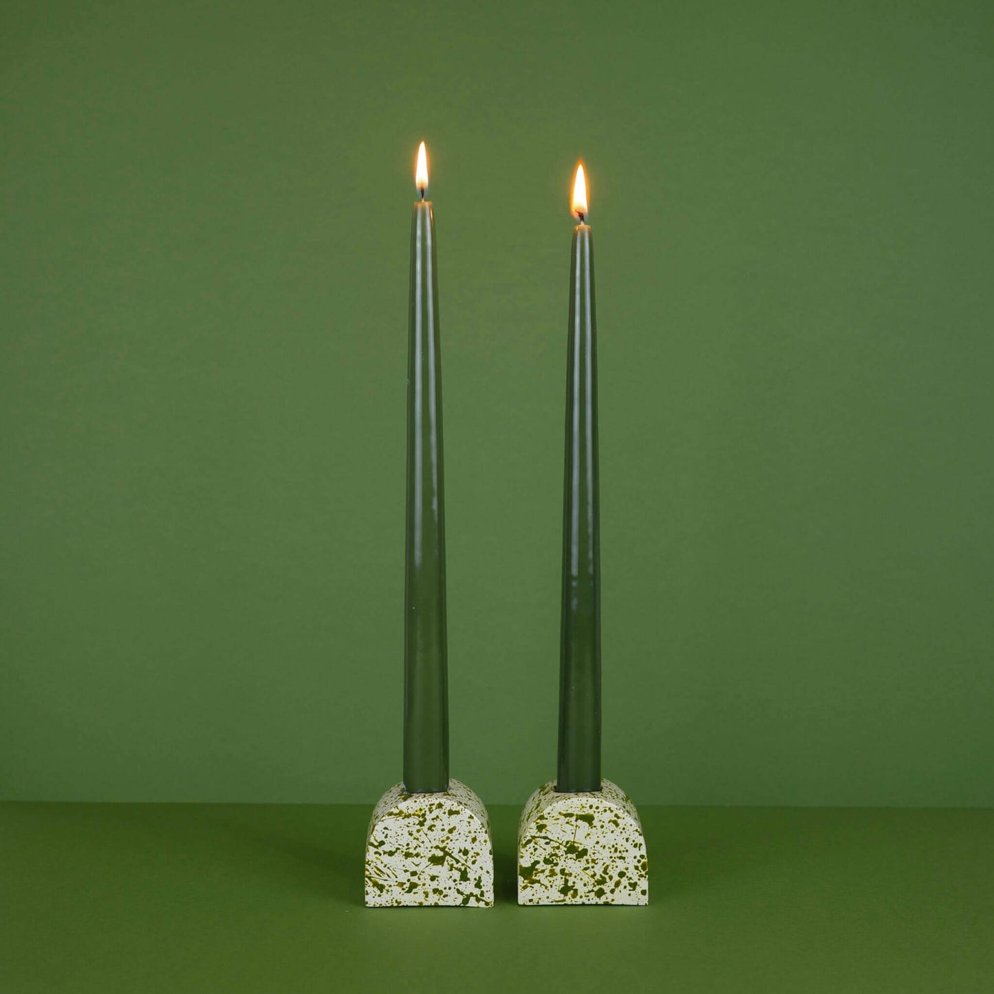 Green paint splattered on a cream concrete small and large arch shaped candleholder